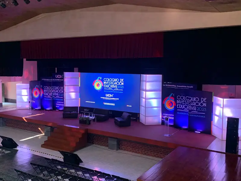 Escenario de un auditorio con pantalla LED central, columnas iluminadas y butacas antes del evento