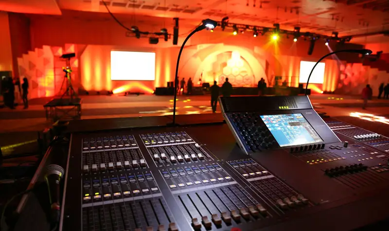 Consola de mezcla de audio en vivo frente a un escenario iluminado