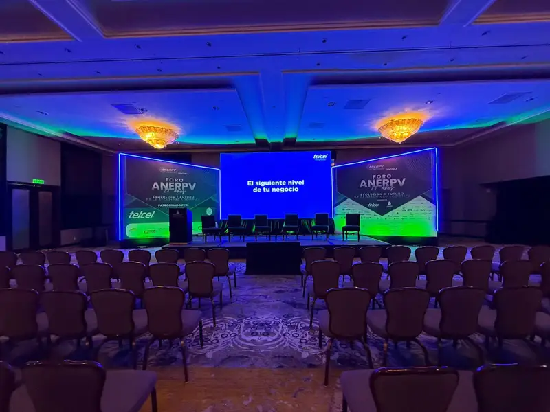 Escenario de foro con tres pantallas e iluminación azul y verde