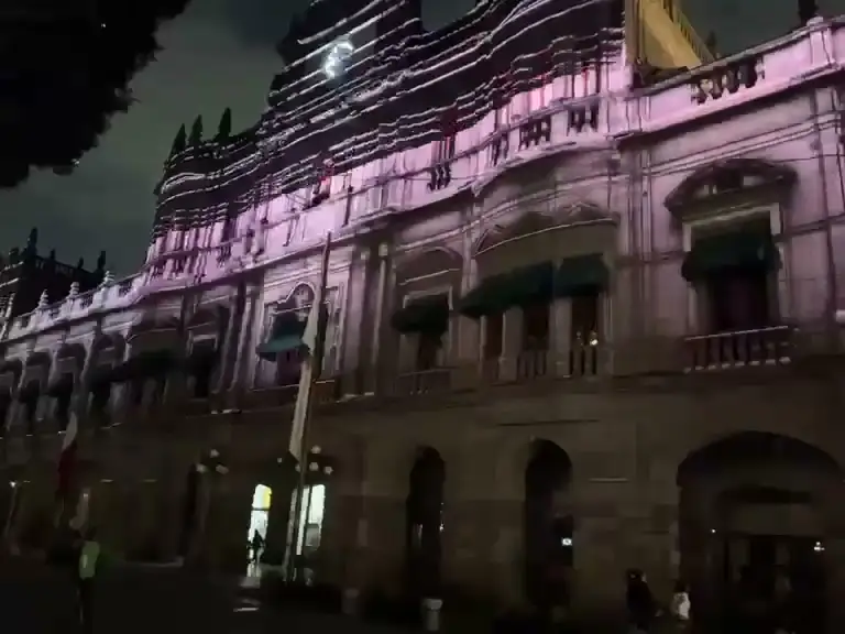Palacio colonial de noche con el primer piso iluminado en rosa por la proyección