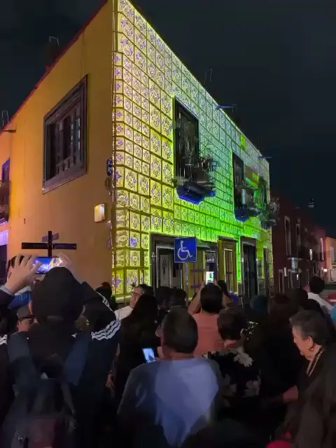 Público en la calle frente a una fachada con mapping en tonos verdes y amarillos